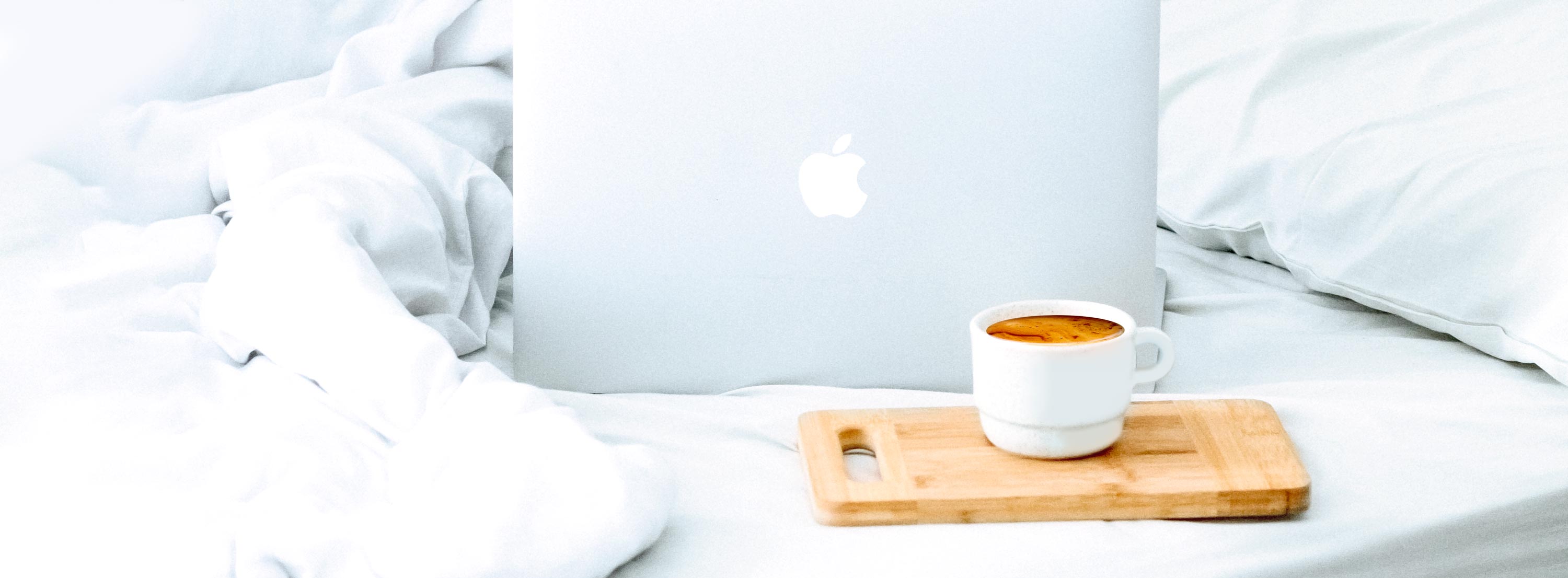 Laptop und Kaffeetasse auf dem Bett: über das Coaching für eine bessere Work-Life-Balance